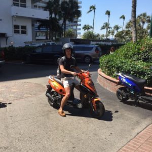 A young man sitting on a orange rental scooter.